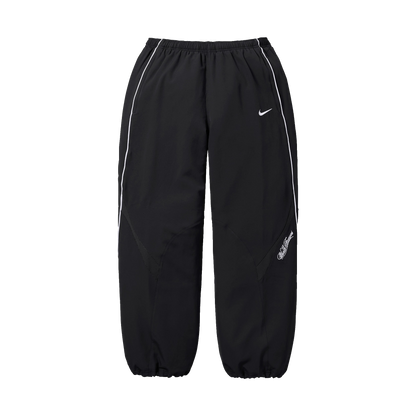 Supreme Nike Track Pant SS25 v čiernom prevedení - pohľad spredu. Výrazné sú voľný strih, elastický pás a charakteristické logo Nike Swoosh na pravej nohavici. Tepláky majú moderný oversized look s elastickými manžetami v dolnej časti.